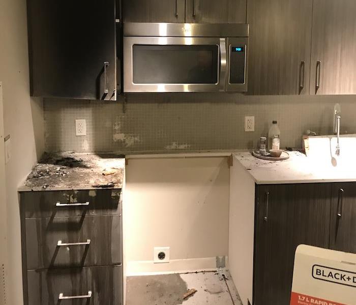 Kitchen with stove removed and charred items on cabinet tops
