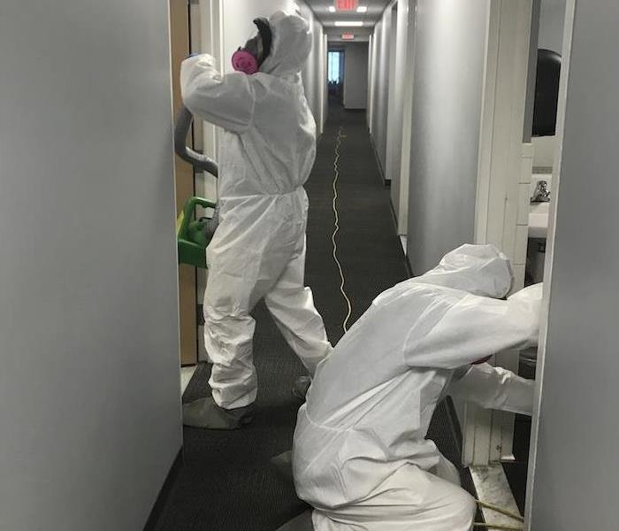 2 male employees in protective gear cleaning a hallway
